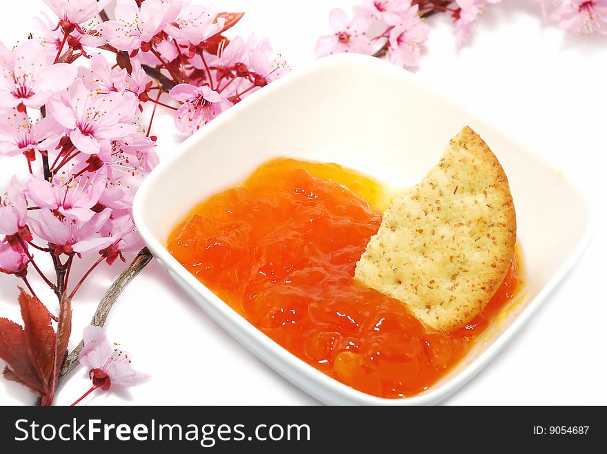 Apricot marmalade in the cup with cracker on the cherry blossoms isolated on the white. Apricot marmalade in the cup with cracker on the cherry blossoms isolated on the white.