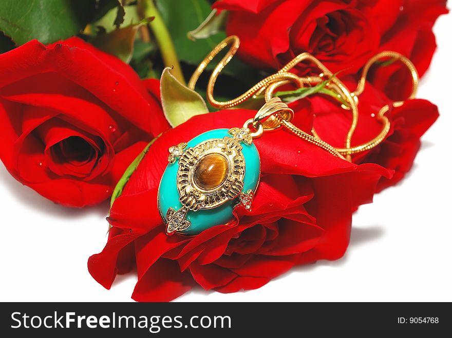 Blue gold Pendant on the red rose with gold chain isolated on the white. Blue gold Pendant on the red rose with gold chain isolated on the white