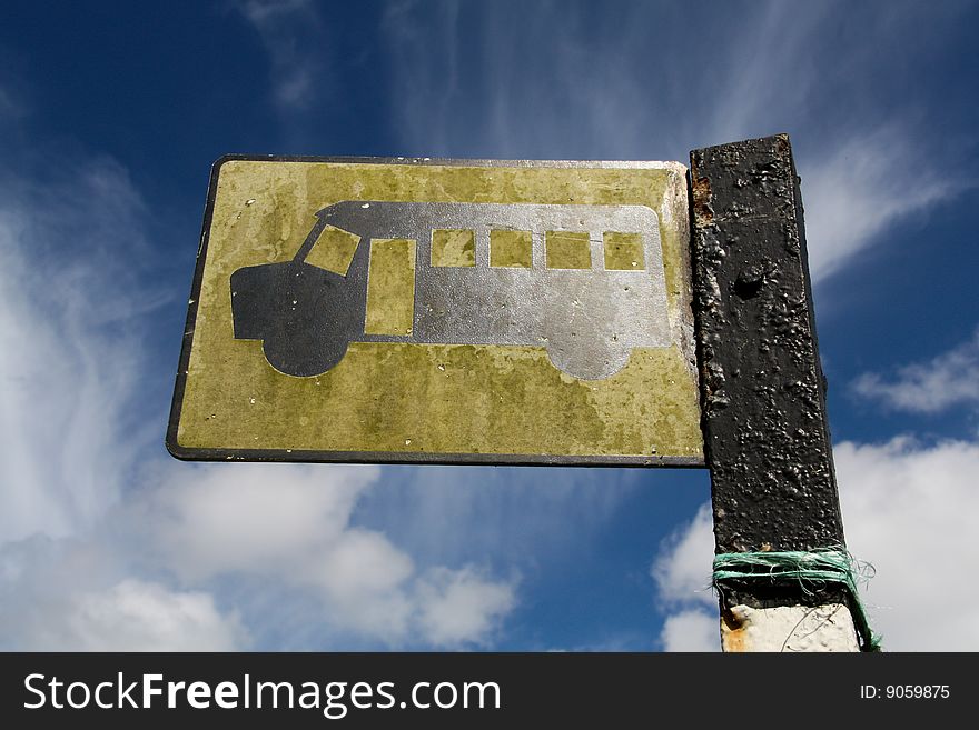 Looking up at a yellow bus stop sign against a blue sky