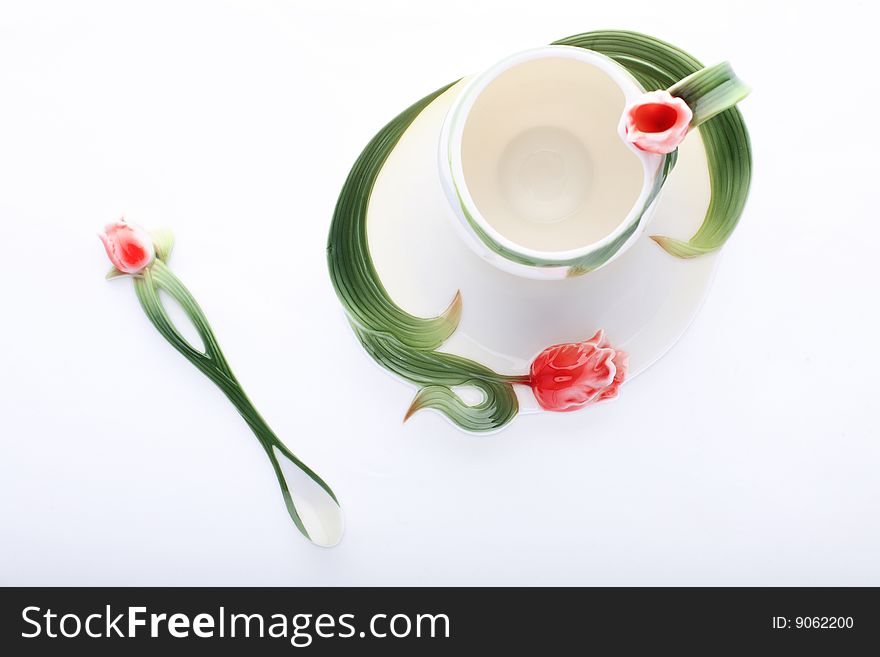 Isolated saucer, cup and spoon decorated with red flower and green color. Isolated saucer, cup and spoon decorated with red flower and green color