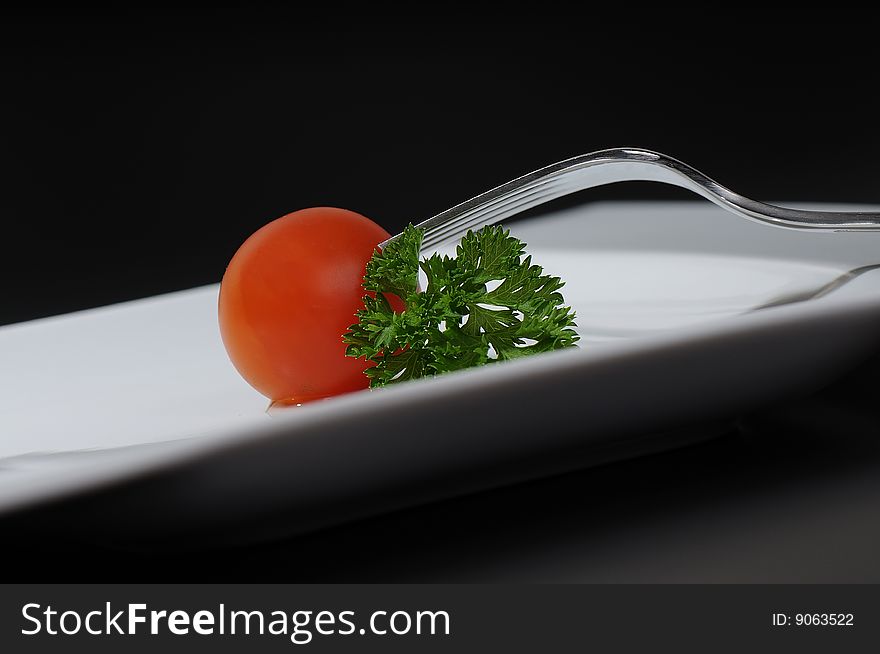 Baby tomato with parsley touched by the fork on white plate. Baby tomato with parsley touched by the fork on white plate