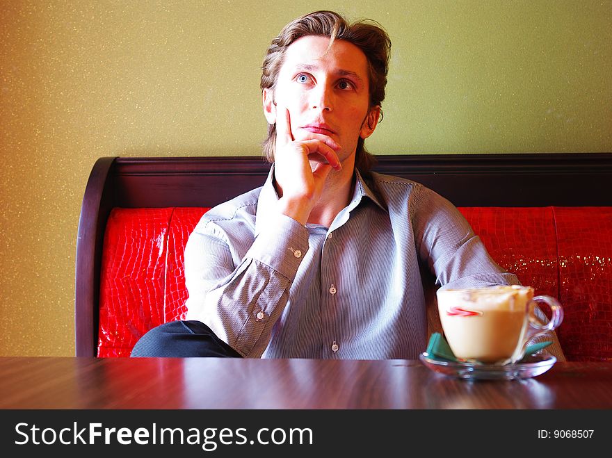 Cup of coffee and young man in modern cafe interior