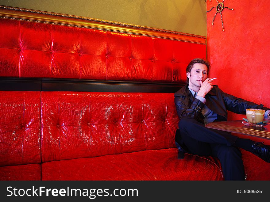 Man's sitting at the cafe's table with cup of cappucino and cigarette. Man's sitting at the cafe's table with cup of cappucino and cigarette