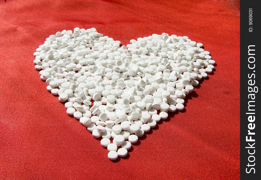 Heart from pills on red silk fabric.