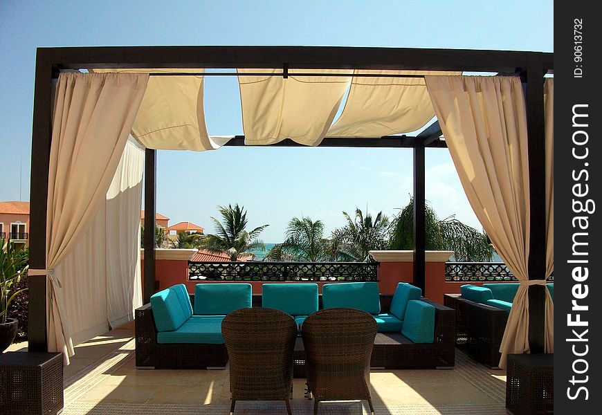 A pergola-style gazebo with curtains and chairs on a terrace. A pergola-style gazebo with curtains and chairs on a terrace.
