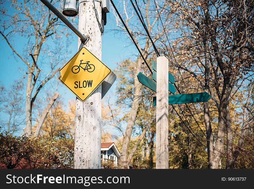 Yellow sign nailed to wooden post with text "slow" in uppercase black letters and the sign includes an image of a cycle, blue sky background. Yellow sign nailed to wooden post with text "slow" in uppercase black letters and the sign includes an image of a cycle, blue sky background.