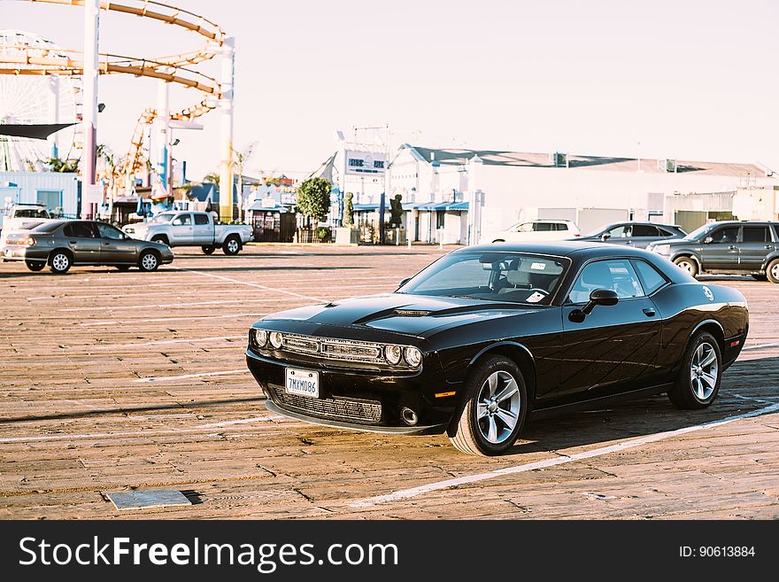 A muscle car on a parking lot with an amusement park on the background.