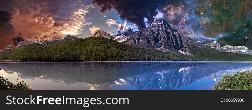 Mountain beside placid lake at dawn with dramatic orange and white clouds and blue sky and reflections in the lake. Mountain beside placid lake at dawn with dramatic orange and white clouds and blue sky and reflections in the lake.