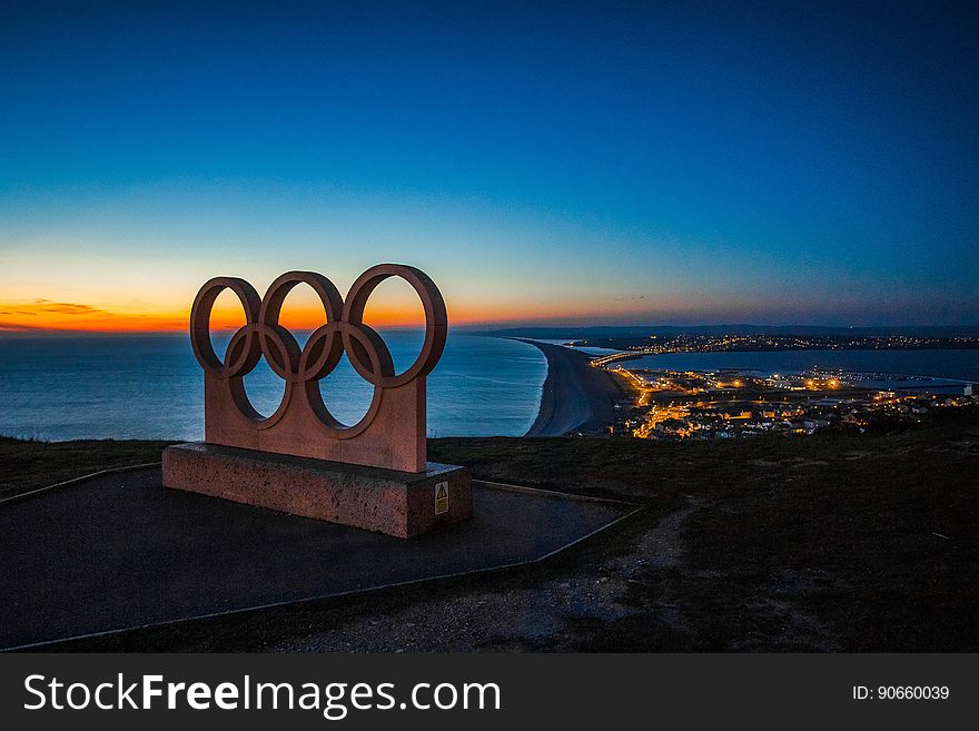 The olympic rings on a hill overlooking a city at night.