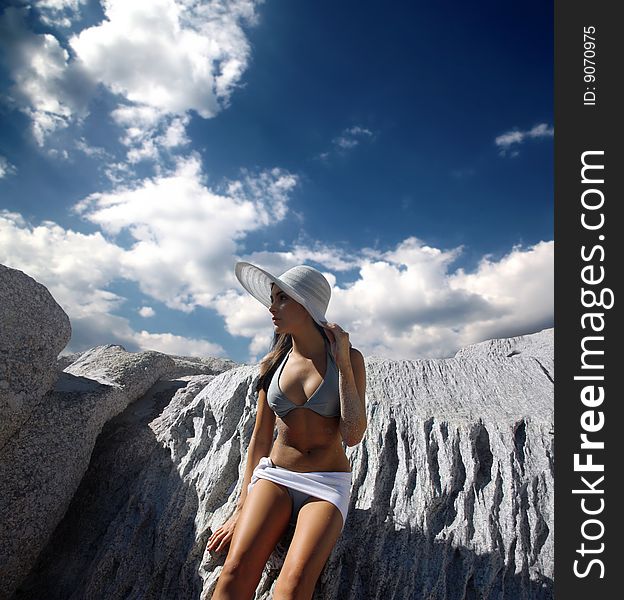 Pretty woman in bikini with hat standing against a searock