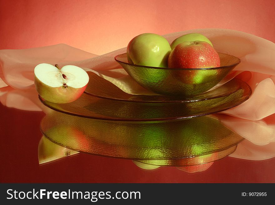 Green apples, ware, pink fabric on a red background and their reflection. Green apples, ware, pink fabric on a red background and their reflection