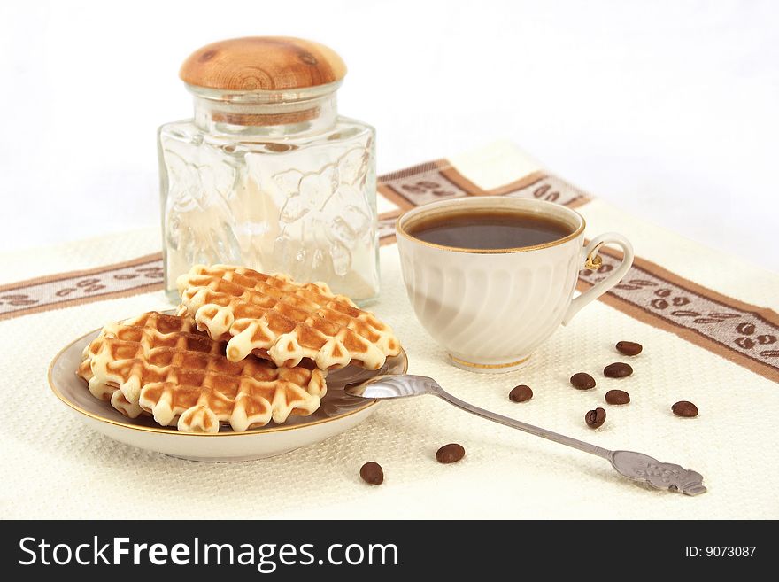 Wafers on a saucer, a porcelain cup from coffee, glass jar, grains, a teaspoon on a napkin. Wafers on a saucer, a porcelain cup from coffee, glass jar, grains, a teaspoon on a napkin