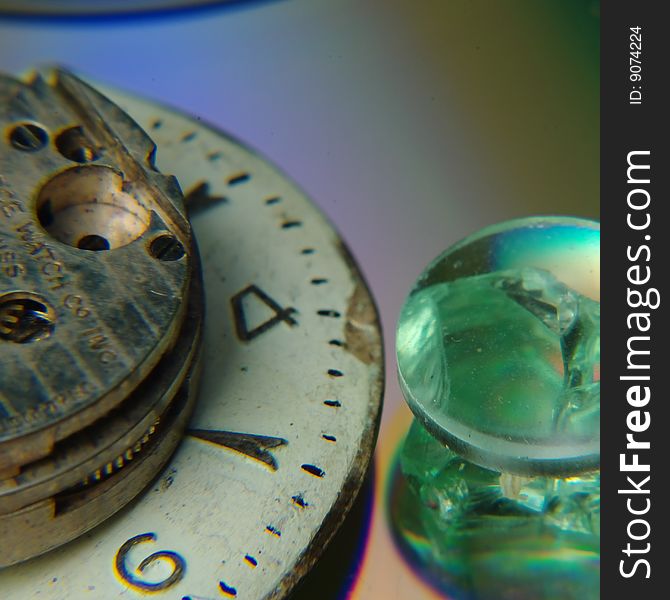 Three parts of old watches are placed on a cd and a piece of broken glass showcasing the intricate workings of an almost lost craftsmanship.  A crystal sits next to a large watchface with the workings sitting on top. Three parts of old watches are placed on a cd and a piece of broken glass showcasing the intricate workings of an almost lost craftsmanship.  A crystal sits next to a large watchface with the workings sitting on top.