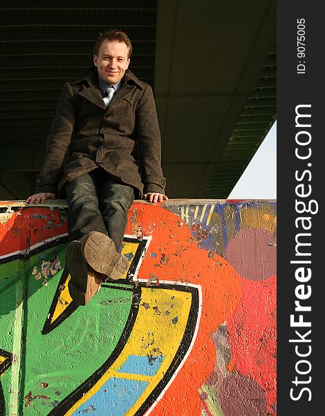 Happy man sitting on the graffiti wall under the bridge. Happy man sitting on the graffiti wall under the bridge