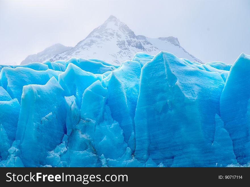 Close up of blue glacial ice in mountains against cloudy or overcast skies.