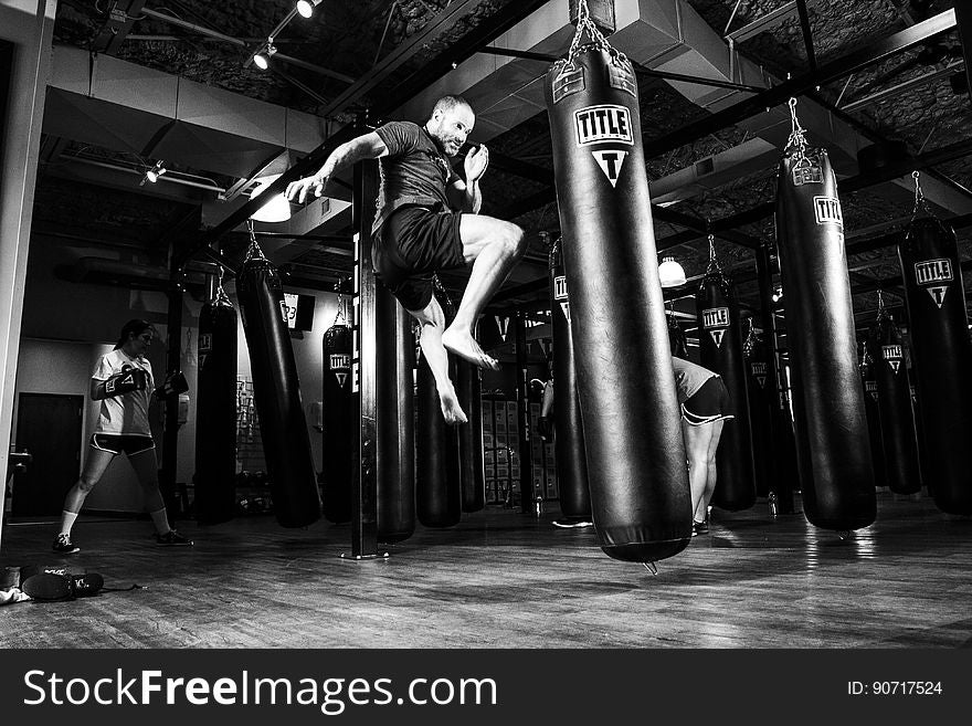 Man practicing kick boxing against bag inside gym in black and white. Man practicing kick boxing against bag inside gym in black and white.