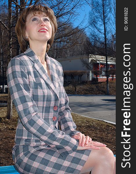 Stylish young woman - lady in checkered (chequered) suit sit on the bench. Stylish young woman - lady in checkered (chequered) suit sit on the bench.