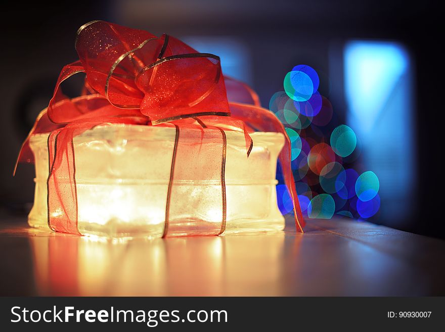 Clear glass gift box illuminated at night with red bow inside house with bokeh Christmas lights. Clear glass gift box illuminated at night with red bow inside house with bokeh Christmas lights.