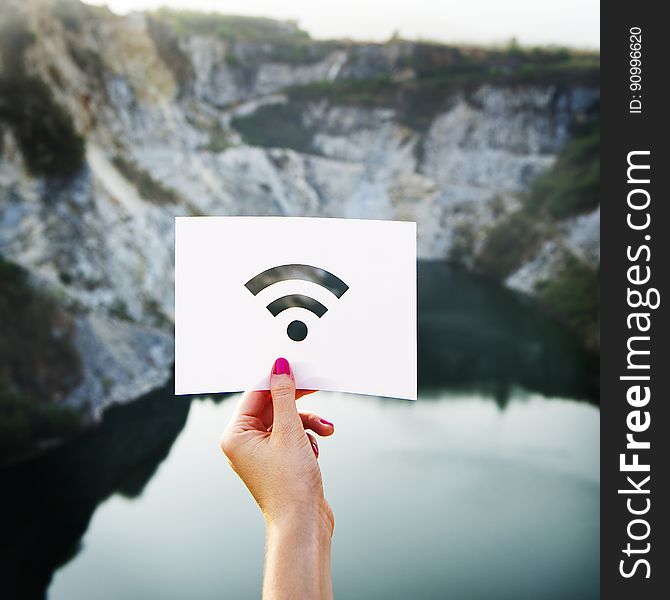 A woman holding up a paper with cut-out wifi sign against the rocky landscape.