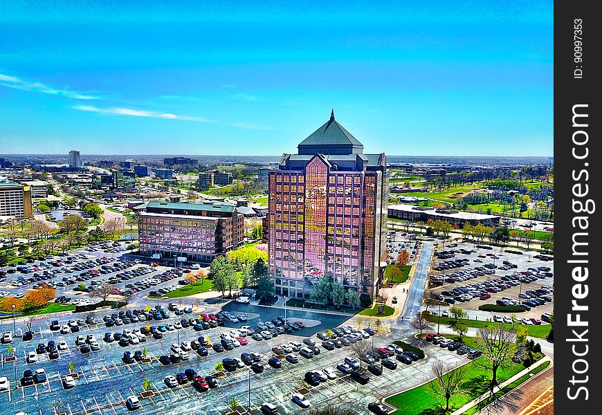 Aerial view of high rise building surrounded by parking lot against blue skies on sunny day.