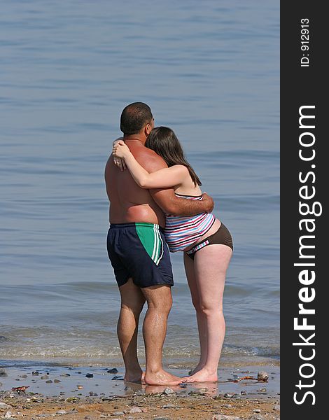 Mixed race couple at the beach of a pregnant female and her partner with their arms around each other, standing barefoot at the shoreline. Mixed race couple at the beach of a pregnant female and her partner with their arms around each other, standing barefoot at the shoreline.