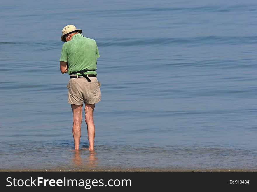 Elderly man paddling at the beach and looking at something in the water. Elderly man paddling at the beach and looking at something in the water.