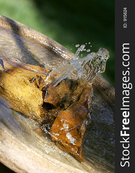 Angled close-up of a peaceful fountain in sunlight and shade, with petrified wood and pool of water (shallow focus). Angled close-up of a peaceful fountain in sunlight and shade, with petrified wood and pool of water (shallow focus).