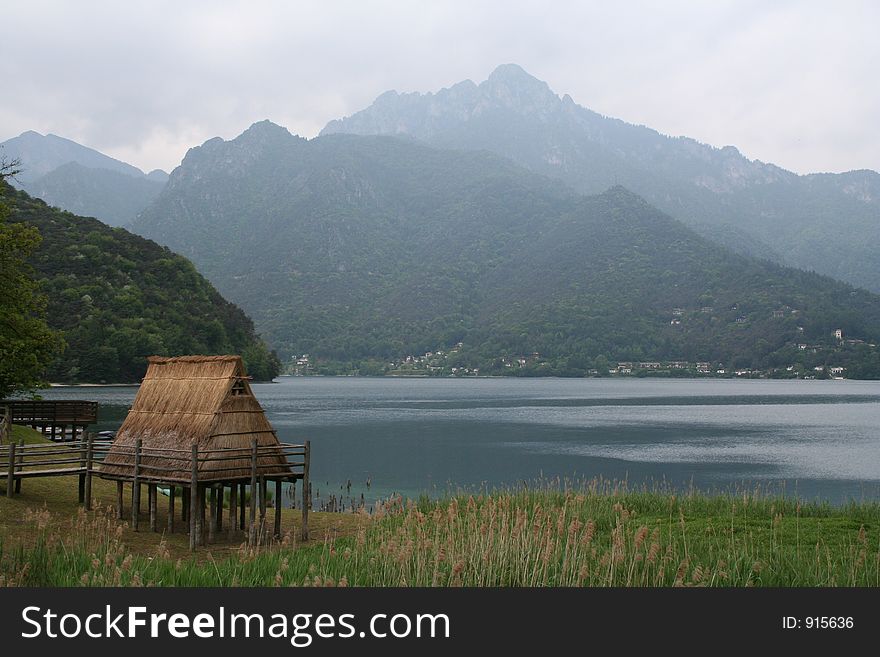 A primitive thatched hut by a lake in the Italian Alps. Landscape shot in misty conditions lends authenticity and atmosphere. A primitive thatched hut by a lake in the Italian Alps. Landscape shot in misty conditions lends authenticity and atmosphere.