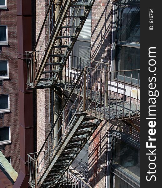 Old fire escape on apartment building, in bright sunshine showing two levels and part of the back of the brick building. Old fire escape on apartment building, in bright sunshine showing two levels and part of the back of the brick building