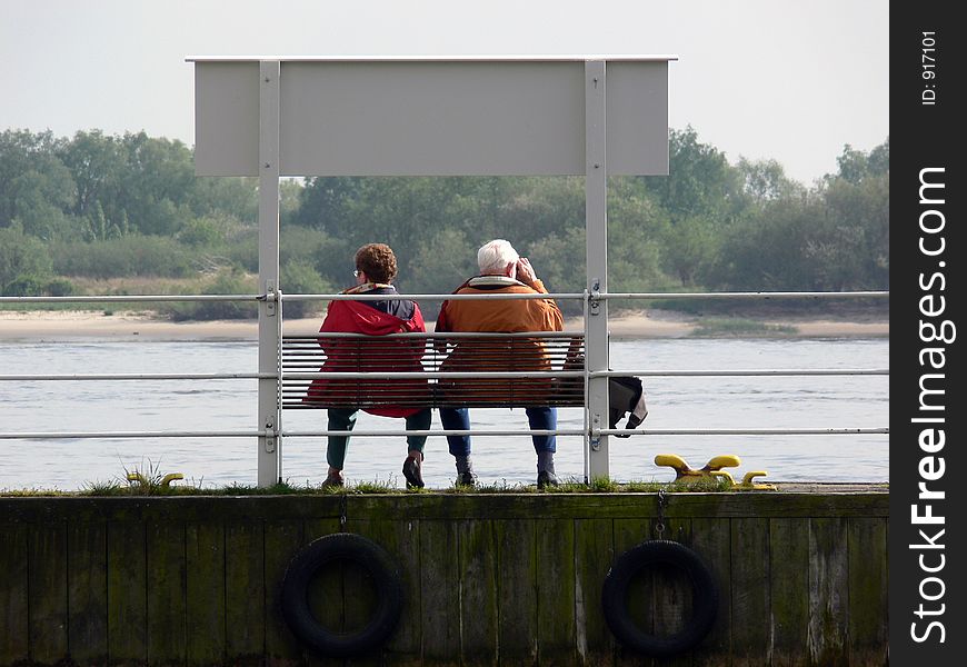 Man and woman watching ships passing by sitting on a bench on a pontoon. Man and woman watching ships passing by sitting on a bench on a pontoon
