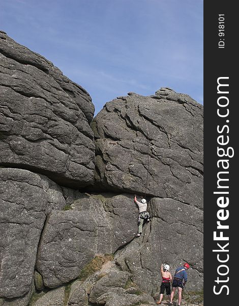 Man climbing rockface with couple feeding ropes. Man climbing rockface with couple feeding ropes