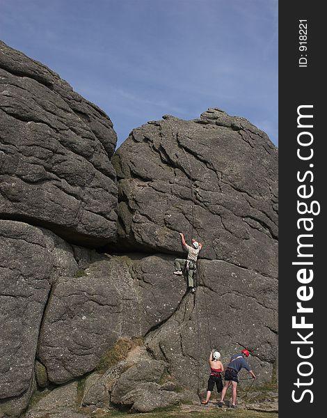 Man climbing rock face with companions below. Man climbing rock face with companions below