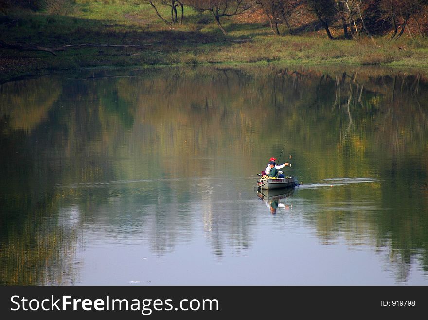 Men fishing in a lake.  They are in a rowboat and there are beautiful reflections in the water. Men fishing in a lake.  They are in a rowboat and there are beautiful reflections in the water.