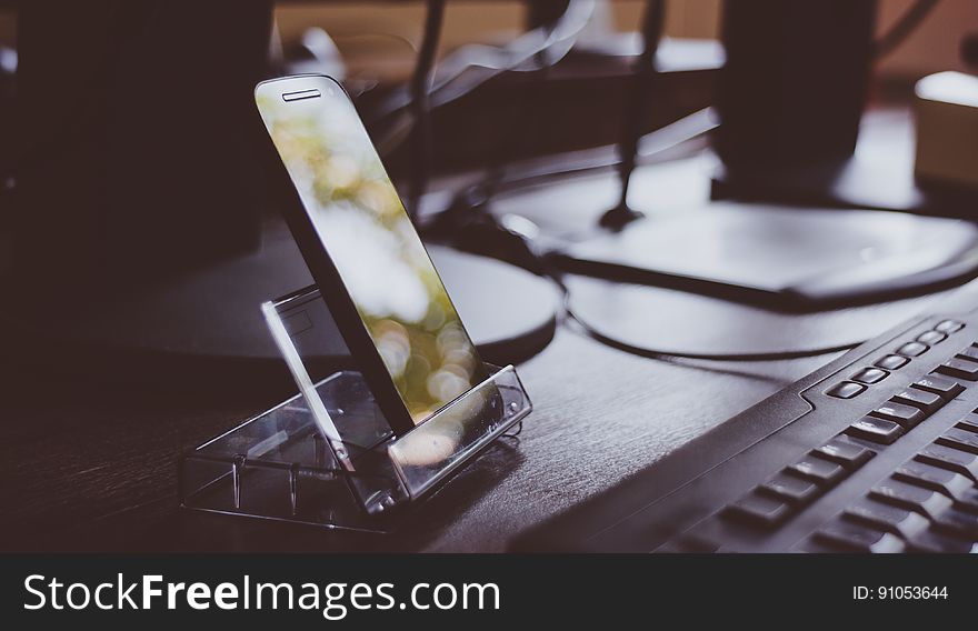 Smartphone in stand next to keyboard on desk. Smartphone in stand next to keyboard on desk.