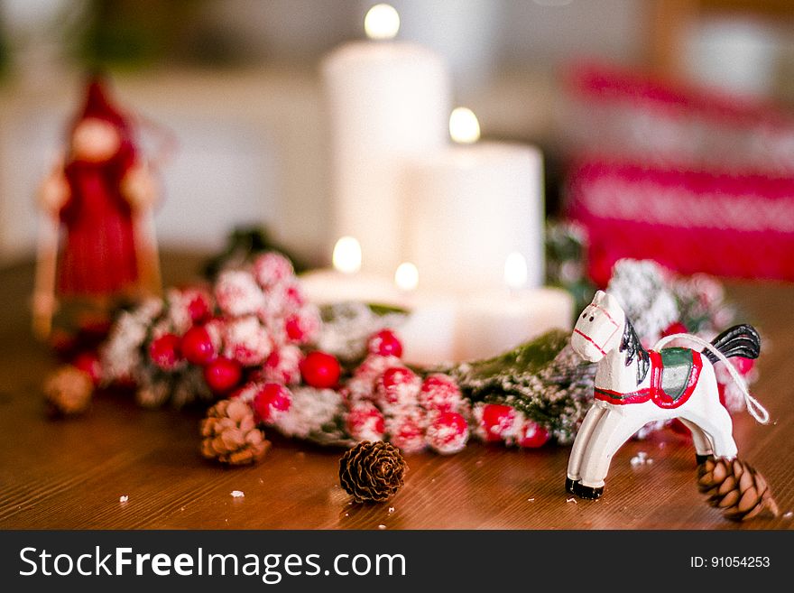 Christmas ornaments around white candles with pine cones on wooden table.