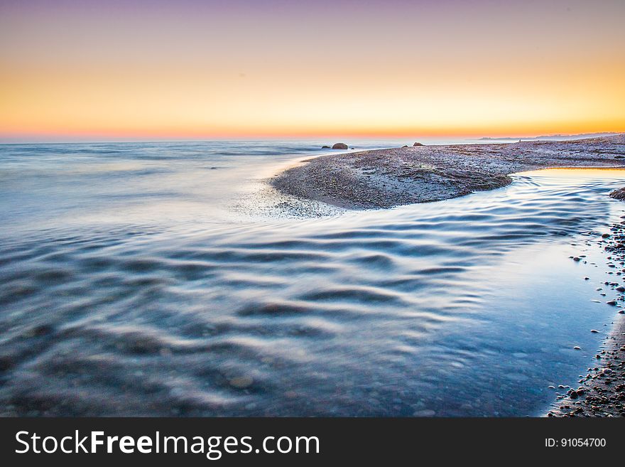 Waves on sandy beach at sunset.