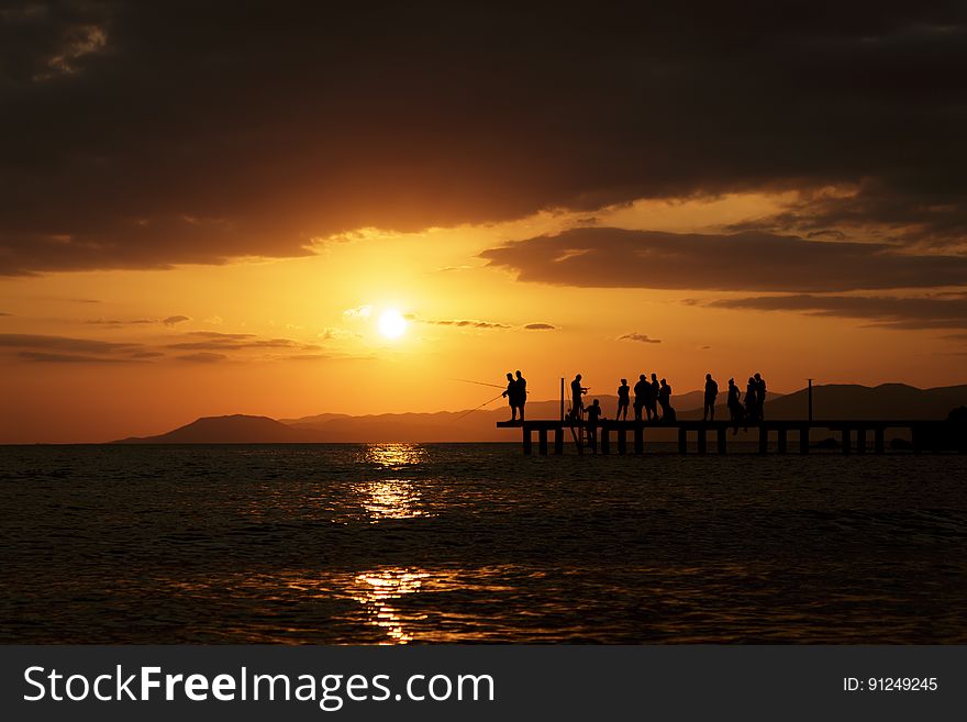 Silhouette of people standing on platform along waterfront at sunset. Silhouette of people standing on platform along waterfront at sunset.