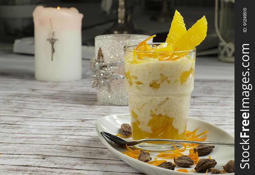 Breakfast fruit parfait in clear glass on white plate with oranges and nuts on rustic tabletop with candles. Breakfast fruit parfait in clear glass on white plate with oranges and nuts on rustic tabletop with candles.