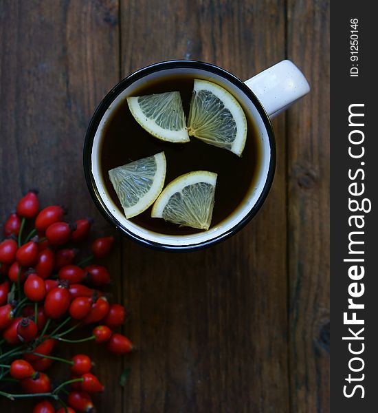 Flat lay of white mug with hot tea and lemon slices next to berries on rustic wooden boards. Flat lay of white mug with hot tea and lemon slices next to berries on rustic wooden boards.