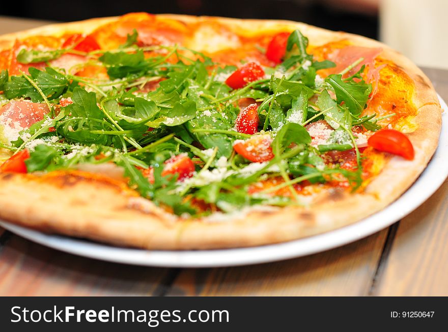 A close up of a pizza with rocket and cherry tomatoes on top. A close up of a pizza with rocket and cherry tomatoes on top.
