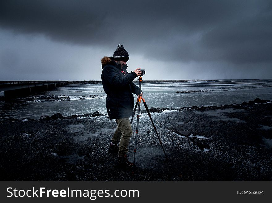 Man in Blue Coat Holding a Tripod With Camera