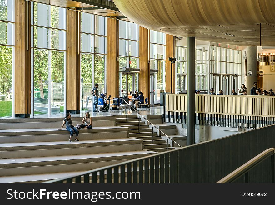 People on steps inside modern contemporary building with glass windows in sunlight. People on steps inside modern contemporary building with glass windows in sunlight.