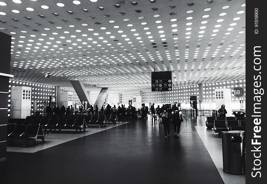 A black and white photo of people at a departure lounge at the airport. A black and white photo of people at a departure lounge at the airport.
