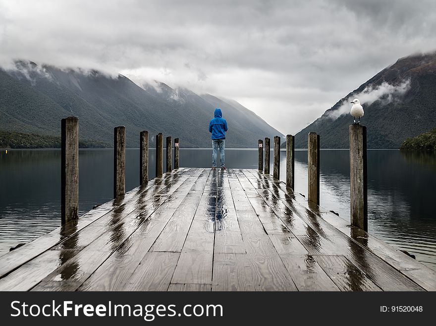 Back of person standing on edge of wooden pier into alpine lake during rain storm. Back of person standing on edge of wooden pier into alpine lake during rain storm.