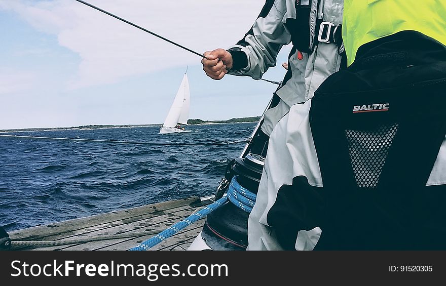A man in a sailing jacket holding a cable on a sailboat. A man in a sailing jacket holding a cable on a sailboat.