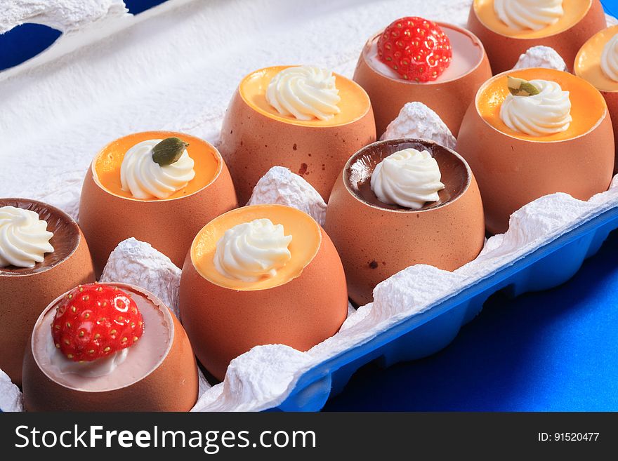 A close up of puddings in eggshells decorated with whipped cream and strawberries.