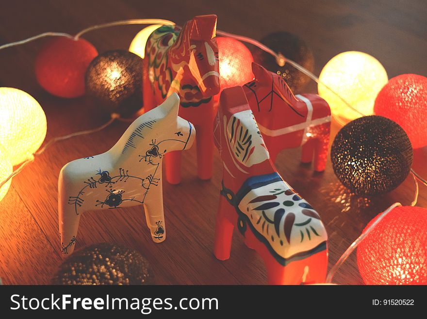 A close up of toy horses and Christmas decorations on a wooden table.