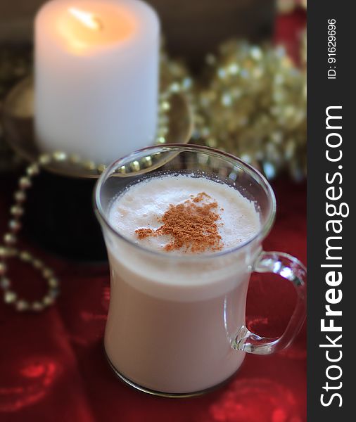 A hot drink in a glass with a candle in the background.