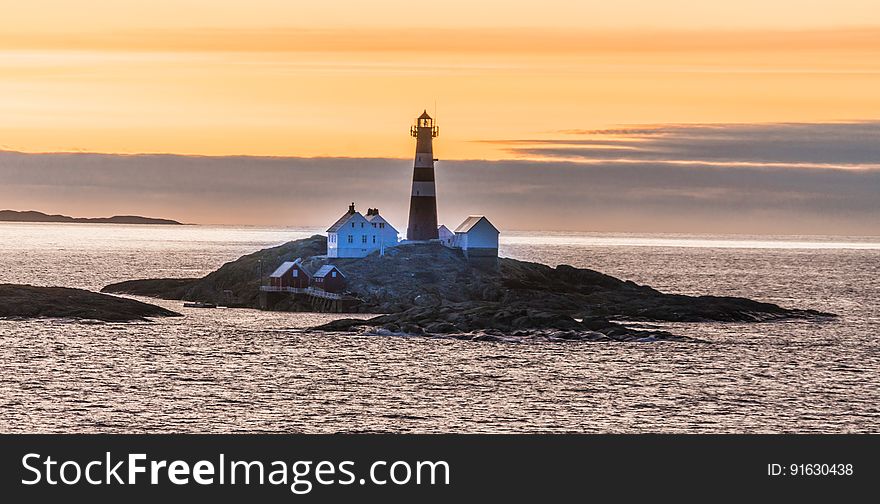 A lighthouse and a few houses on a small rocky island at sunset. A lighthouse and a few houses on a small rocky island at sunset.