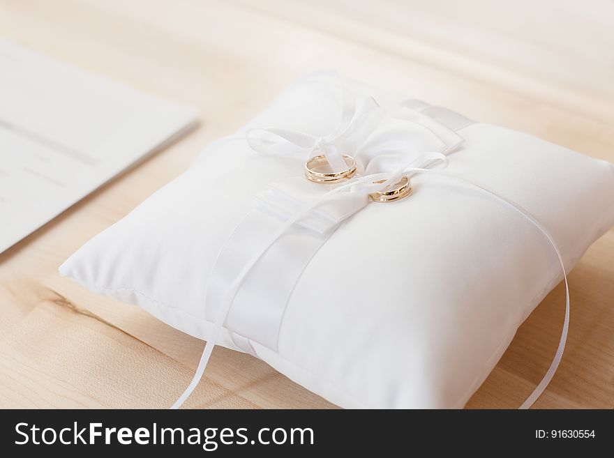 A white pillow with a ribbon and a pair of golden wedding rings on top. A white pillow with a ribbon and a pair of golden wedding rings on top.